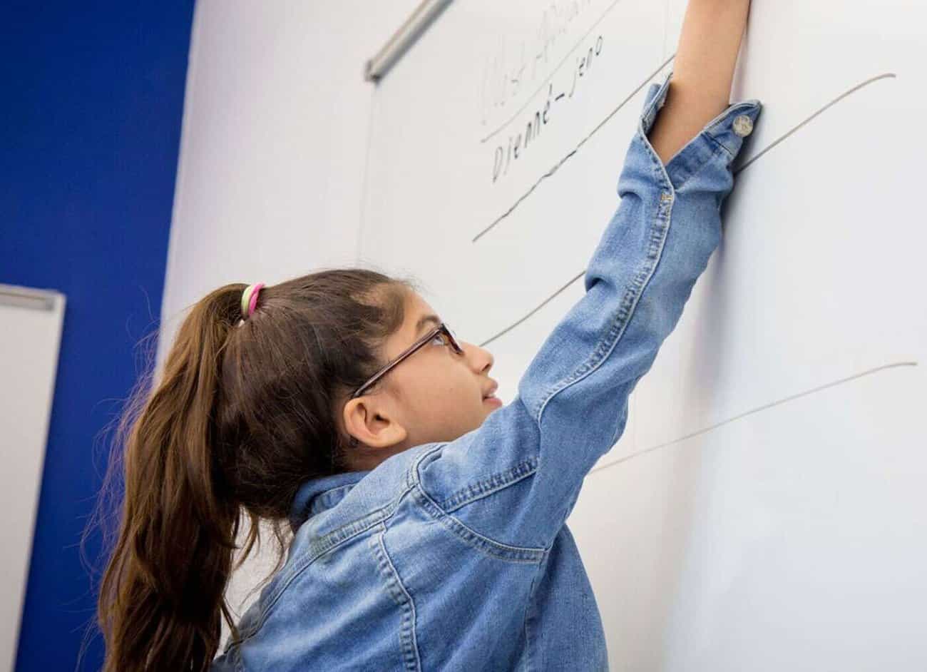 A Selwyn middle school student reaching up to write West African place names on the classroom whiteboard