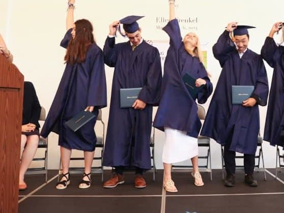 Selwyn graduates in navy caps and gowns turning their tassels on stage, diplomas in hand