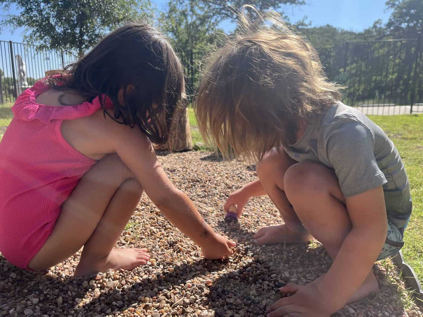 Two Selwyn students crouched side by side outdoors, sifting through gravel together.